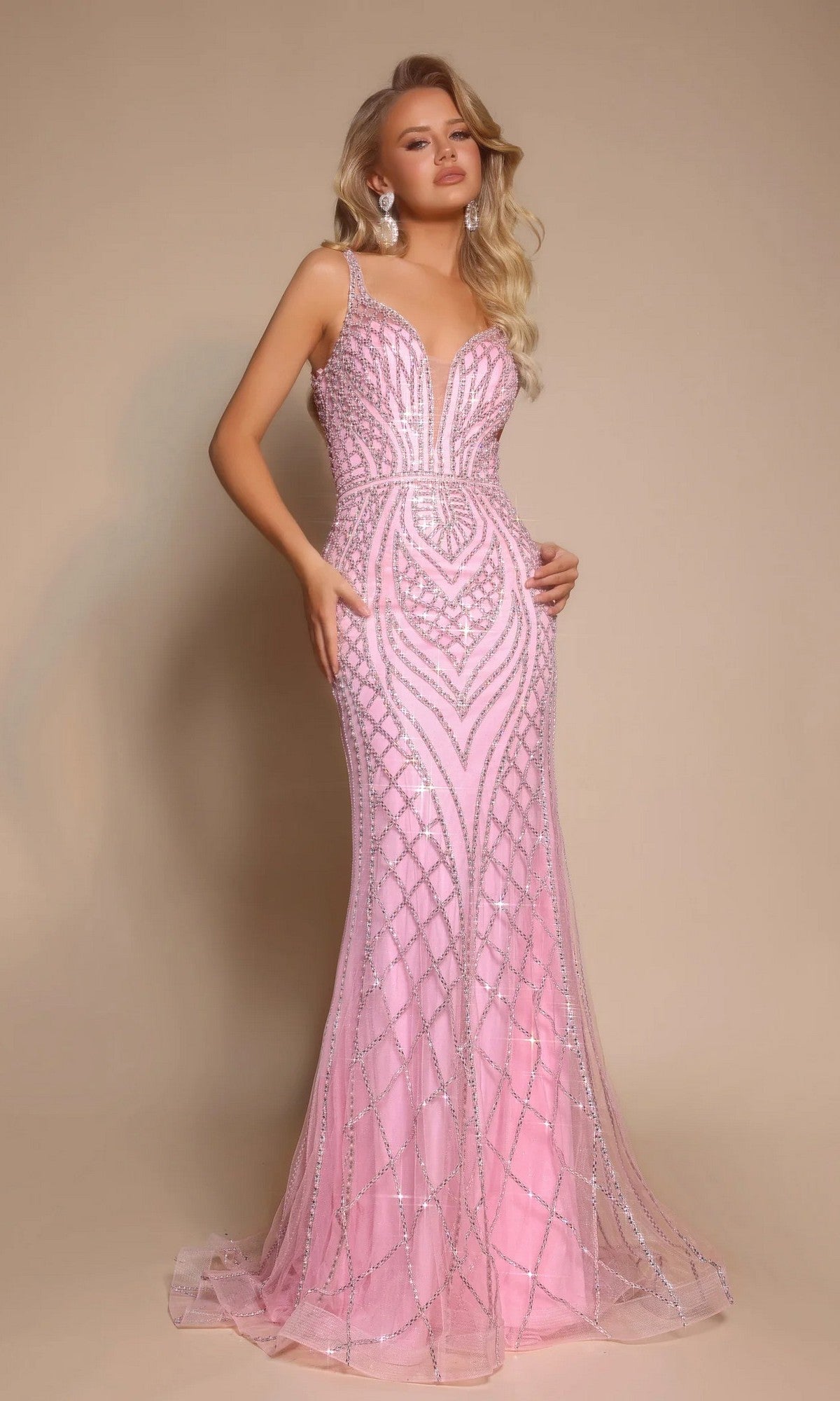 A woman poses against a beige background wearing the Portia and Scarlett PS26089 long formal dress in pink, featuring a floor-length silhouette, intricate geometric beadwork, a deep V neckline, and thin shoulder straps.